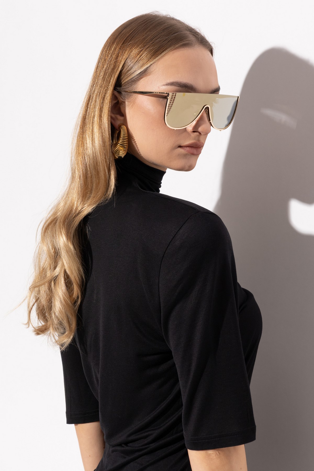 Девушка в крупных зеркальных очках Alaïa с золотистой оправой и черным топом