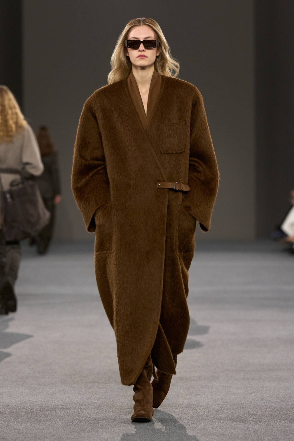 Модель в длинном коричневом пальто с округлыми рукавами на показе Max Mara
